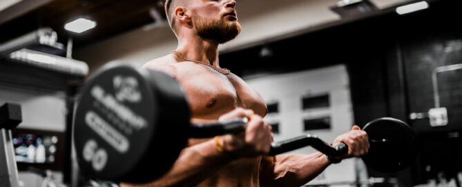 topless man in black shorts carrying black dumbbell