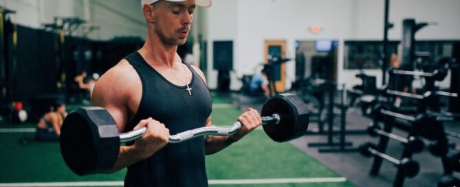 man in black tank top and white cap holding black and gray dumbbell