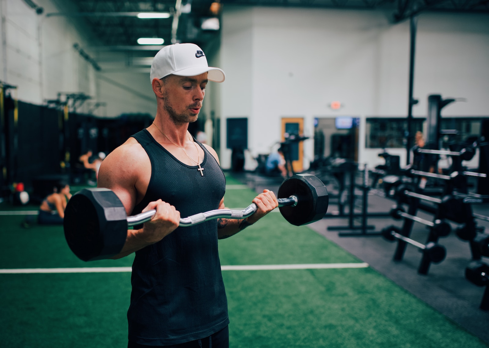 man in black tank top and white cap holding black and gray dumbbell