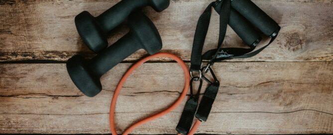 Deux haltères noirs et une bande élastique orange posés sur une surface en bois rustique